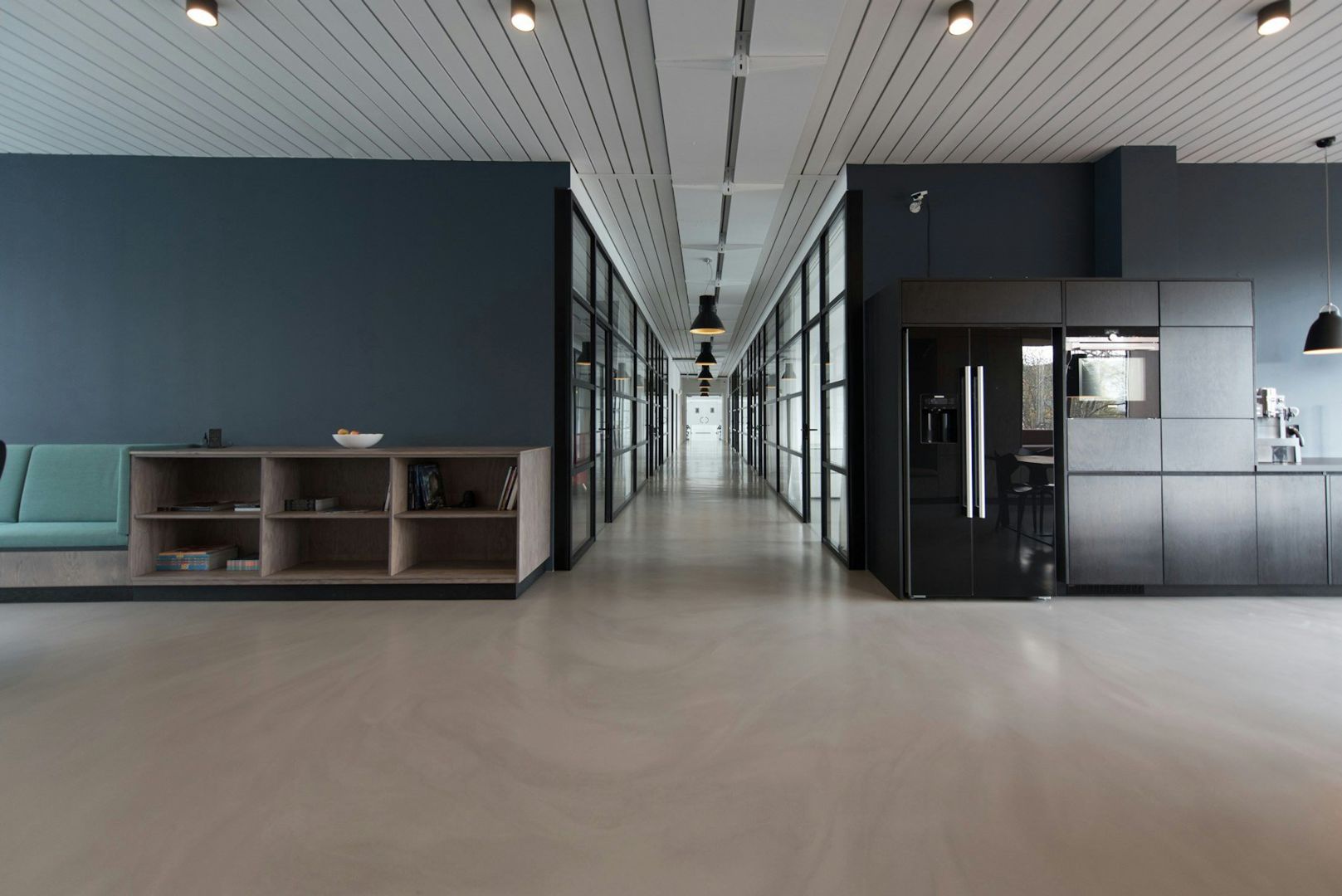 Polished-concrete corridor running between glazed rooms and a dark kitchen