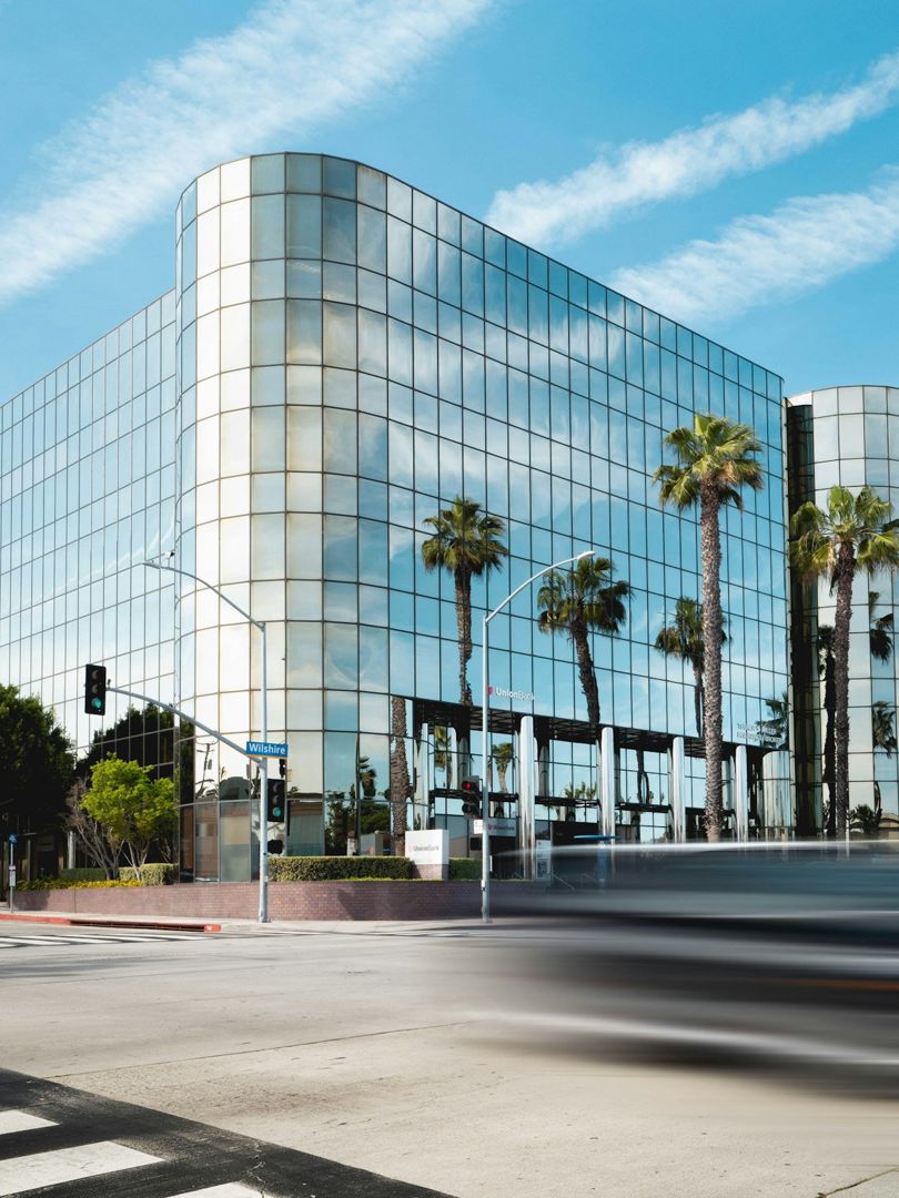 Curved glass facade reflecting palm trees and sky